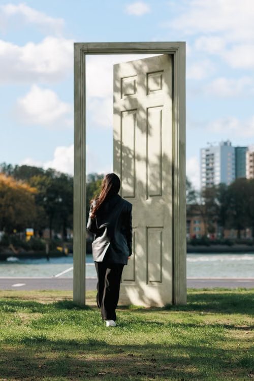 Woman walking through a freestanding open door in a park