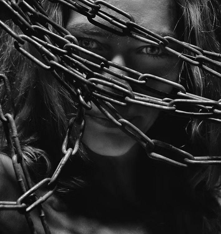 Woman looking out through rusted chains, in black and white