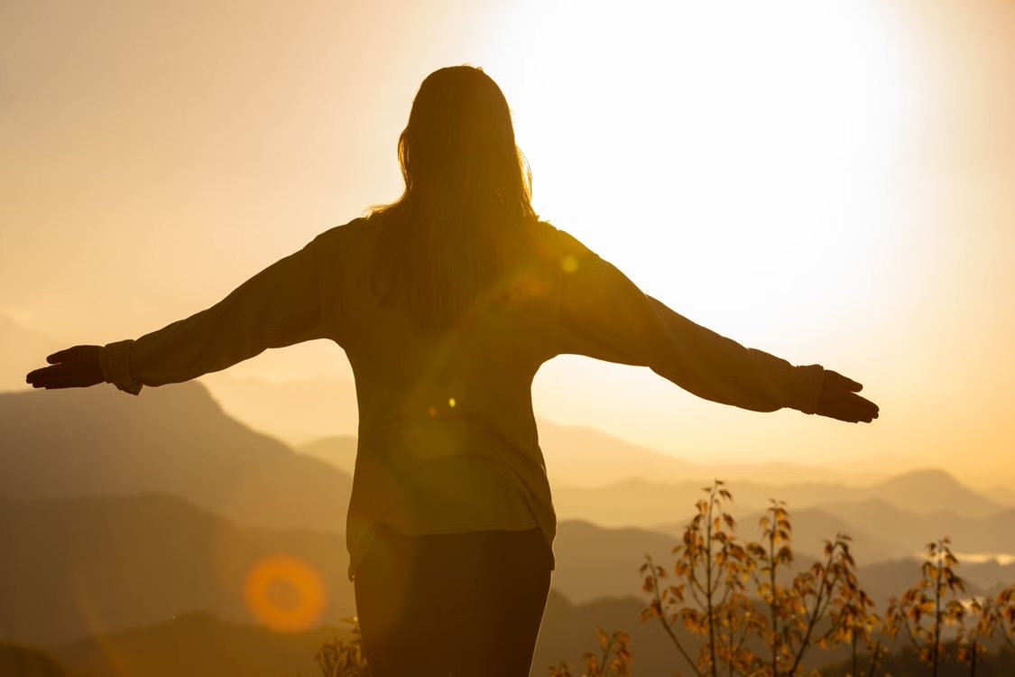 Woman with her arms open toward a sunrise over the mountains